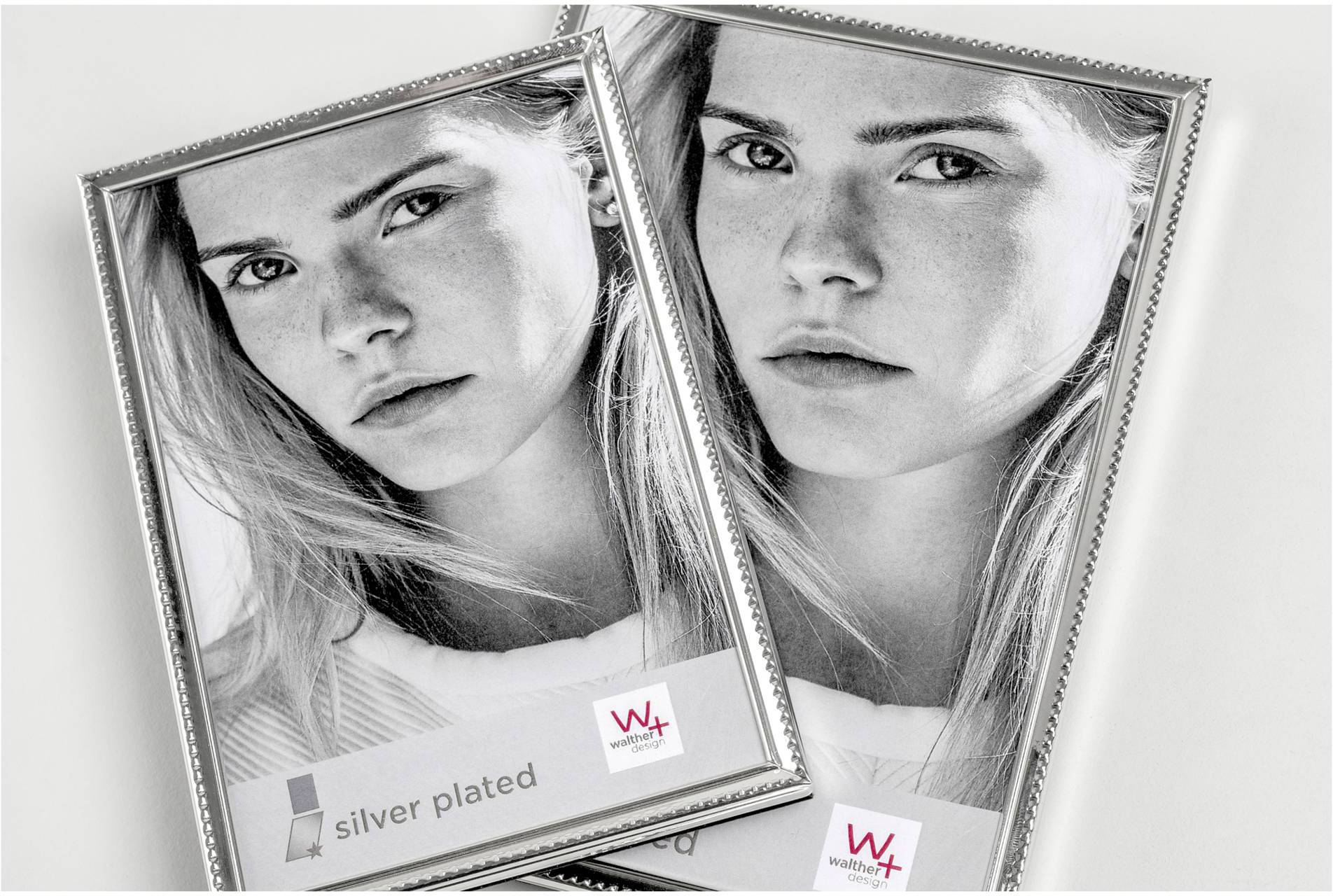 Dva stříbrné fotorámečky leží překrytě. V každém rámečku je stejný černobílý portrét ženy.