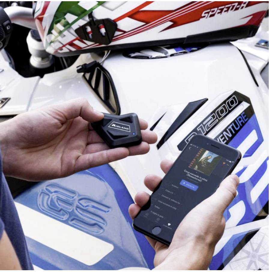 Osoba drží malé zařízení a smartphone s aplikací s názvem 'GO' vedle bílého motocyklu.