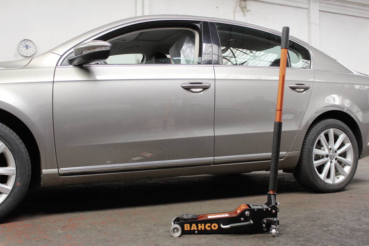 Stříbrné auto stojí v garáži, přímo před ním je na podlaze hydraulický zvedák značky Bahco.