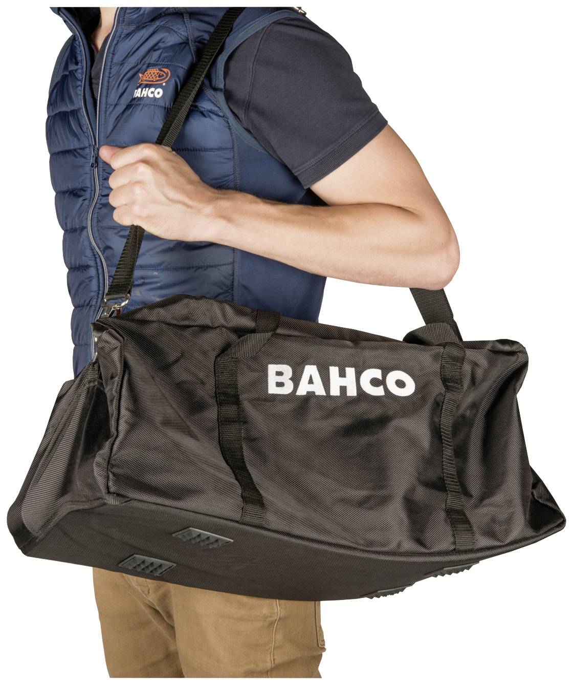 Osoba nese černou tašku BAUCO přes rameno. Taška má velký bílý nápis "BAHCO".