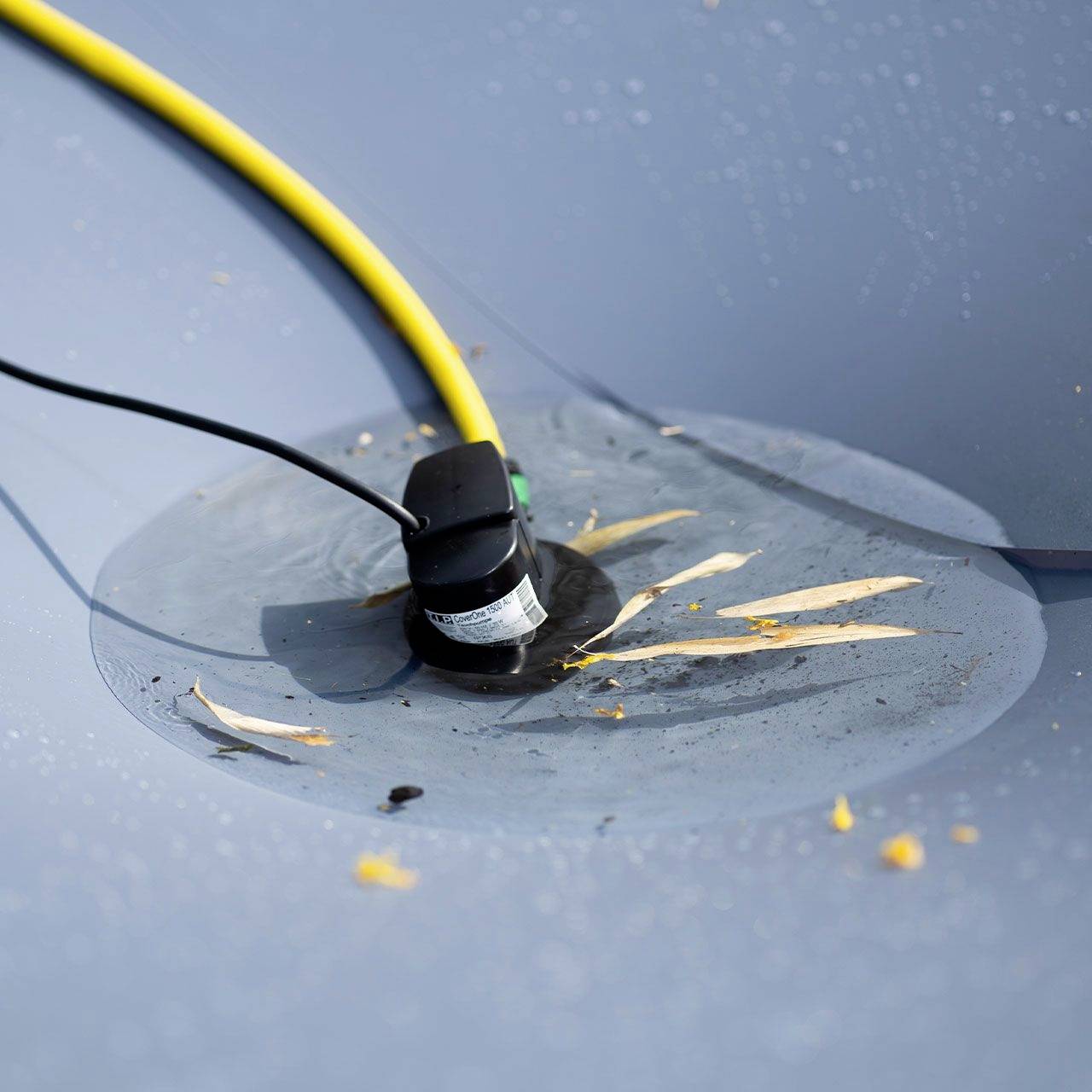 Černý senzor je zabudovaný do hladkého šedého povrchu, obklopený žlutými kabely a malými škrábanci na povrchu.