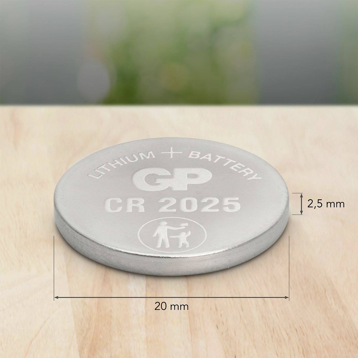 Stříbrná lithiová knoflíková baterie s potiskem "CR 2025", "GP". Uvedené rozměry: průměr 20 mm, výška 2,5 mm. Rozmazané pozadí.