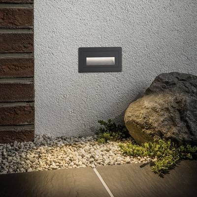 LED venkovní světlo vestavěné do zdi jemně osvětluje podlahu z oblázků a desek vedle skalní rostliny.
