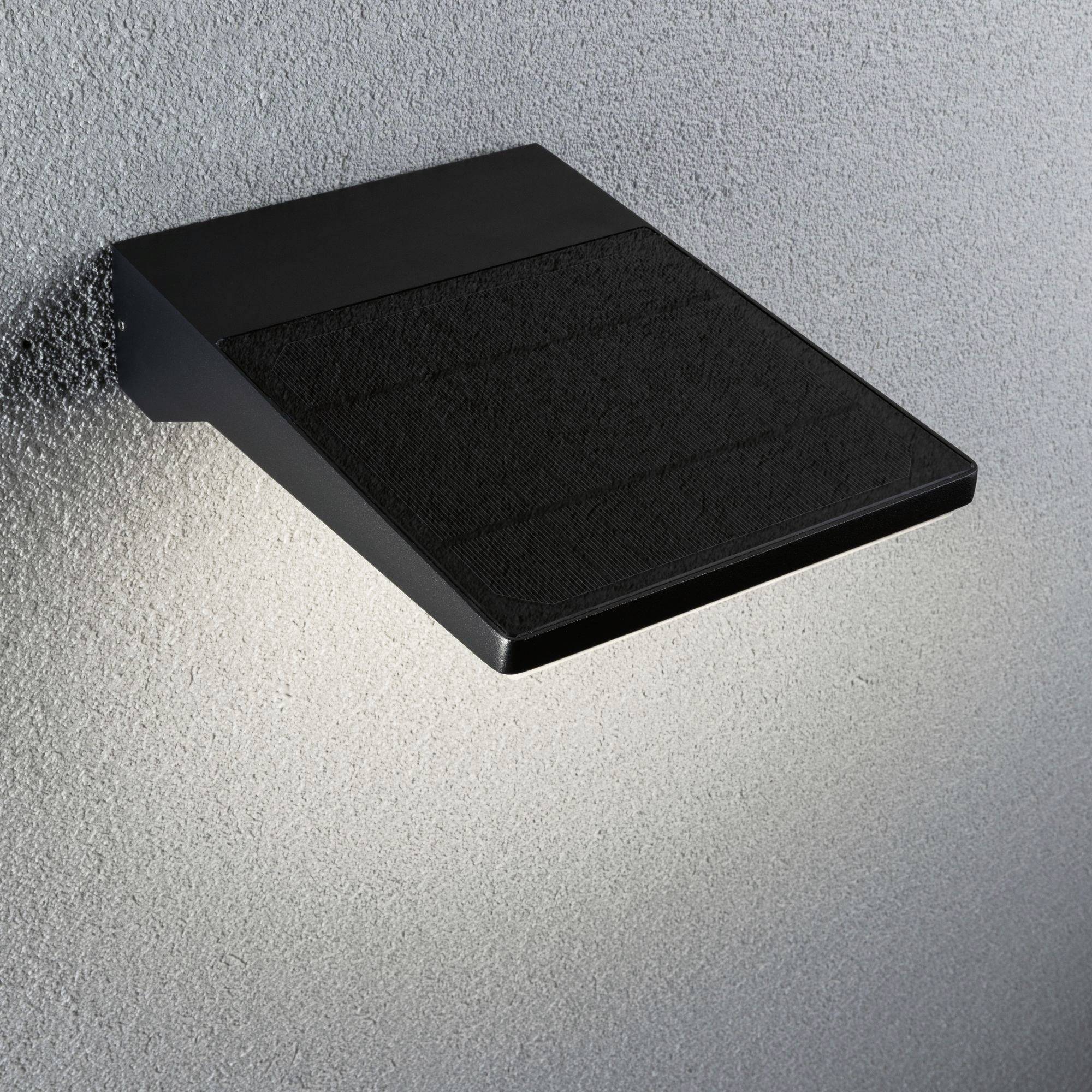 Moderní černé nástěnné svítidlo na šedé zdi, které směrem dolů vyzařuje měkké světlo a vytváří elegantní, minimalistickou atmosféru.
