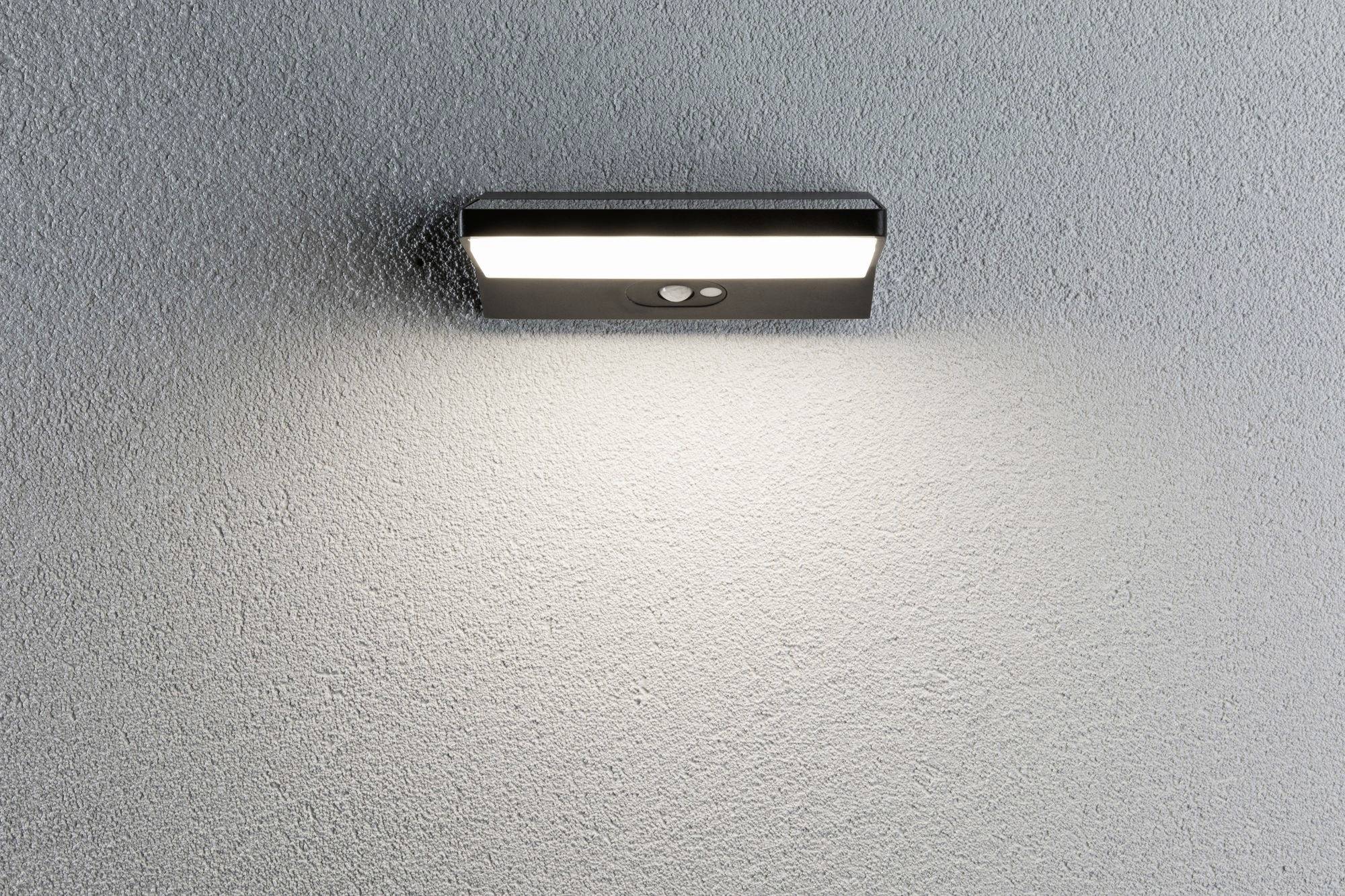 Nástěnná lampa na šedé zdi osvětlující prostor pod ní jasným světlem.