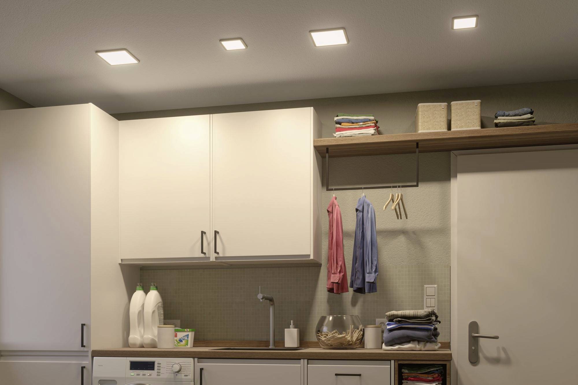Prádelna s pračkou, bílou skříní a nástěnnými policemi s prádlem a čisticími prostředky.