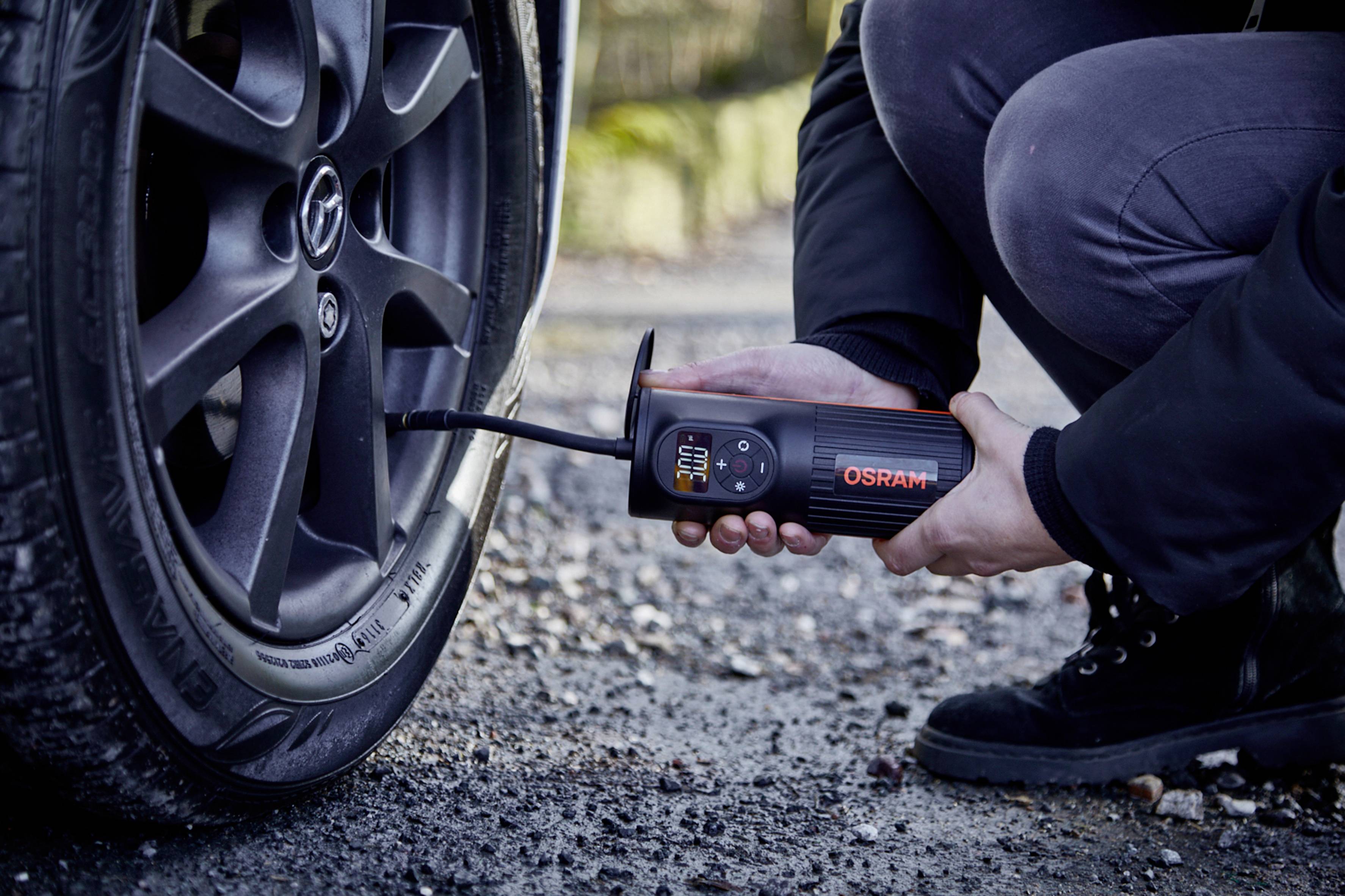 Osoba nafukuje přenosným zařízením pneumatiku automobilu. Zařízení zobrazuje údaje o tlaku vzduchu.