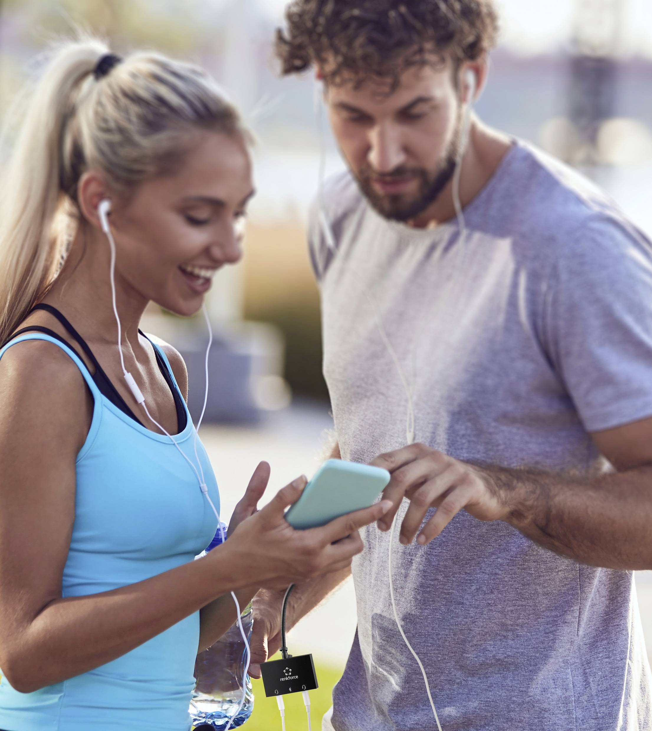 Žena a muž v sportovním oblečení poslouchají hudbu na sluchátkách a společně se dívají na smartphone.