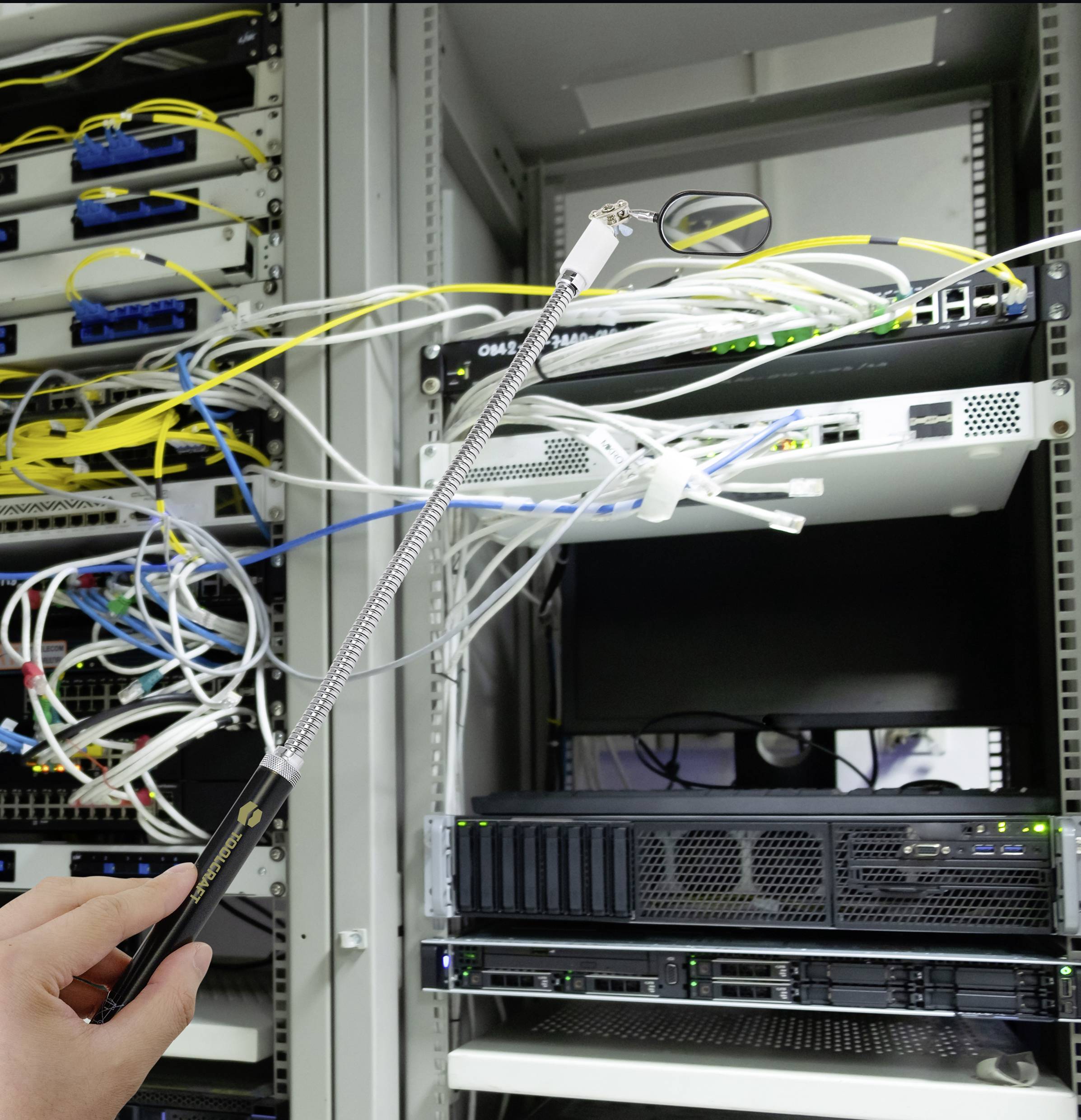 Jedna ruka drží teleskopické zrcadlo před serverovou skříní s síťovými kabely, aby mohla prozkoumat těžko dostupné oblasti.
