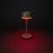 Moderní stolní lampa s červeným světelným odleskem, stojící na tmavém pozadí. Lampa má minimalistický design.