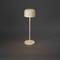 Minimalistická stolní lampa s kulatým stínidlem a štíhlou základnou, stojící na tmavém pozadí.