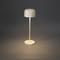 Minimalistická stolní lampa s kulatým, plochým stínidlem. Vyzařuje teplé světlo na šedém pozadí, vhodná pro moderní interiér.