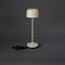 Béžová stolní lampa s jednoduchým, moderním designem a dlouhým, tenkým stojanem. Vedle ní leží volně položený černý kabel.