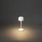 Malá, moderní stolní lampa s kulatým bílým stínidlem osvětluje tmavé pozadí.