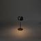 Minimalistická černá stolní lampa na stole, která vyzařuje teplé světlo v temné místnosti.