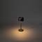 Minimalistická černá stolní lampa měkce svítí na tmavém pozadí.