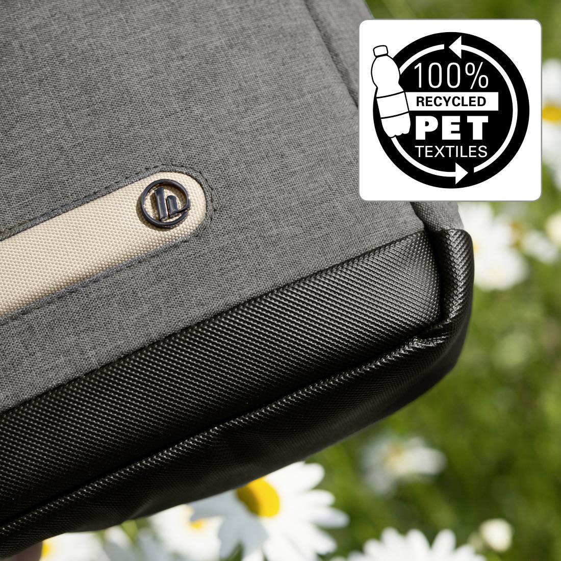 Šedá taška z recyklovaného PET textilu s logem. V pozadí rozostřené květiny. Text na obrázku: '100% recyklovaný PET textil'.
