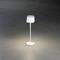 Bílá stolní lampa s úzkým krkem a širokým stínítkem, svítící na tmavém pozadí. Moderní, minimalistický design.