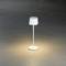 Bílá, moderní stolní lampa na šedé podlaze; rozptyluje měkké, teplé světlo v kruhovém prostoru kolem sebe.
