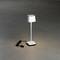 Jednoduchá, moderní stolní lampa v bílé barvě na šedé podlaze. Vedle ní je vidět černý síťový kabel.