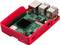 Počítač Raspberry Pi v červeném pouzdře s viditelnými konektory a ventilátorem.