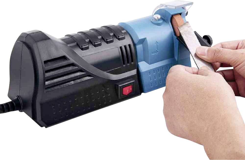 Osoba brousí nůž pomocí elektrického brusku na nože. Nůž je veden oběma rukama.