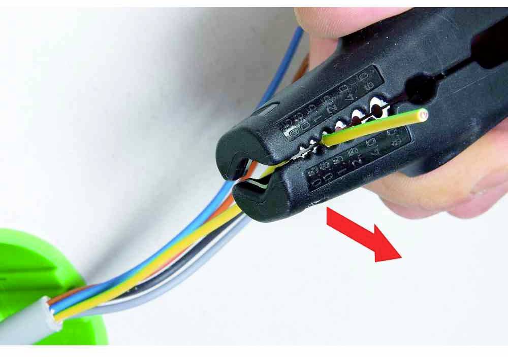 Krimpovací kleště svírají elektrický kabel. Červená šipka ukazuje na místo, kde je kabel zpracováván.