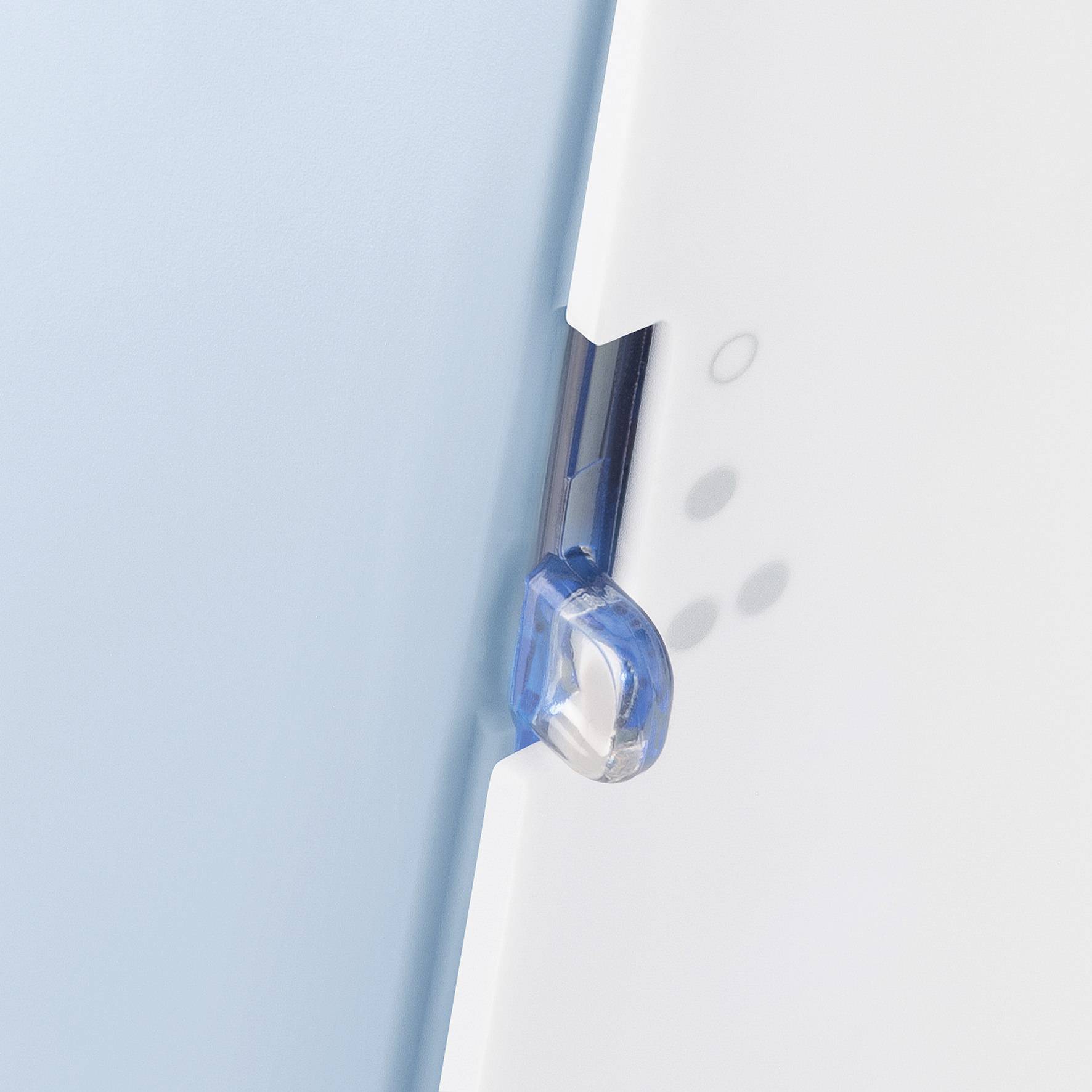 Detailní záběr modrého a bílého předmětu s průhlednou plastovou sponou po straně.