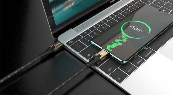 Mobilní telefon leží na klávesnici notebooku a je nabíjen pomocí USB kabelu. Indikátor nabití ukazuje '100%'.