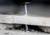 Detailní záběr vrtáku, který vrtá díru do bílé keramické dlaždice. Kolem otvoru je viditelný prach a malé úlomky.