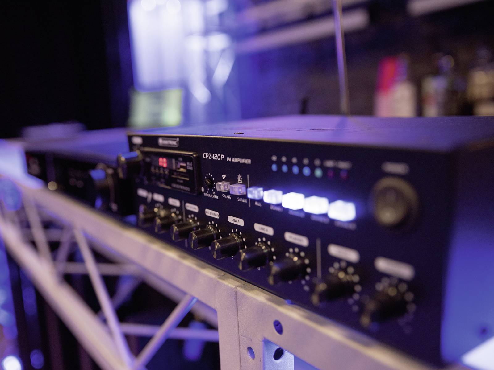 Rackmontovaný audio zesilovač umístěný na polici. Přední panel obsahuje několik přepínačů a světel signalizujících aktivní provoz.