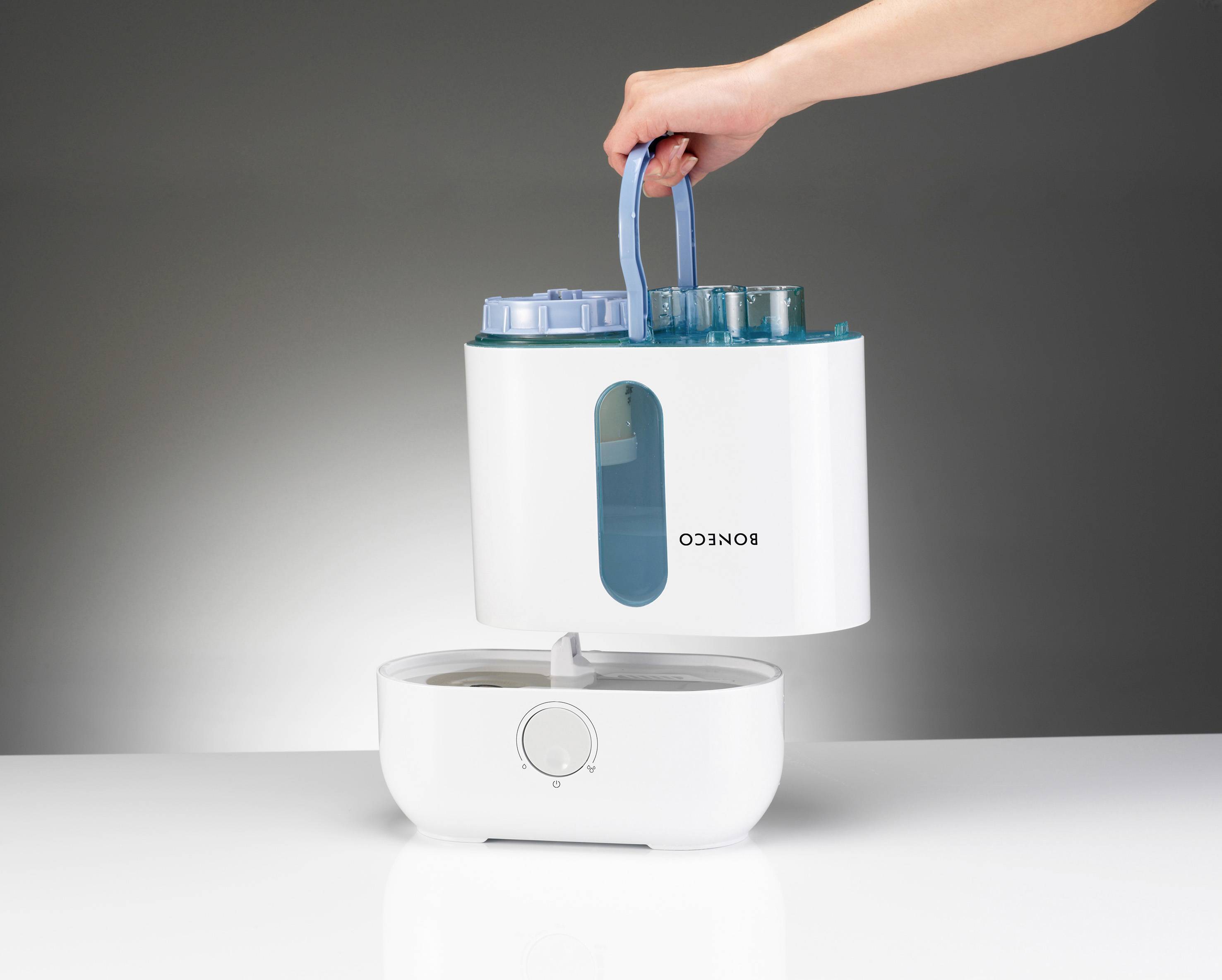 Ruka zvedá nádržku na vodu z klimatizace. Nádržka je průhledně modrá a je vytahována shora.