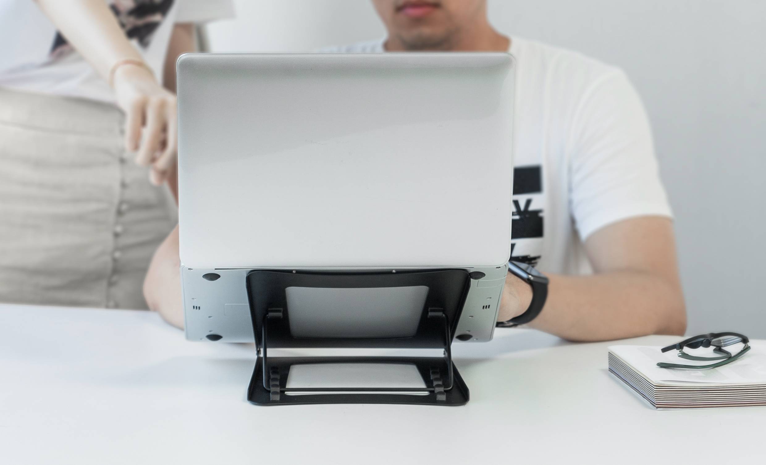 Sedící osoba pracuje na laptopu, zatímco stojící osoba ukazuje na obrazovku.