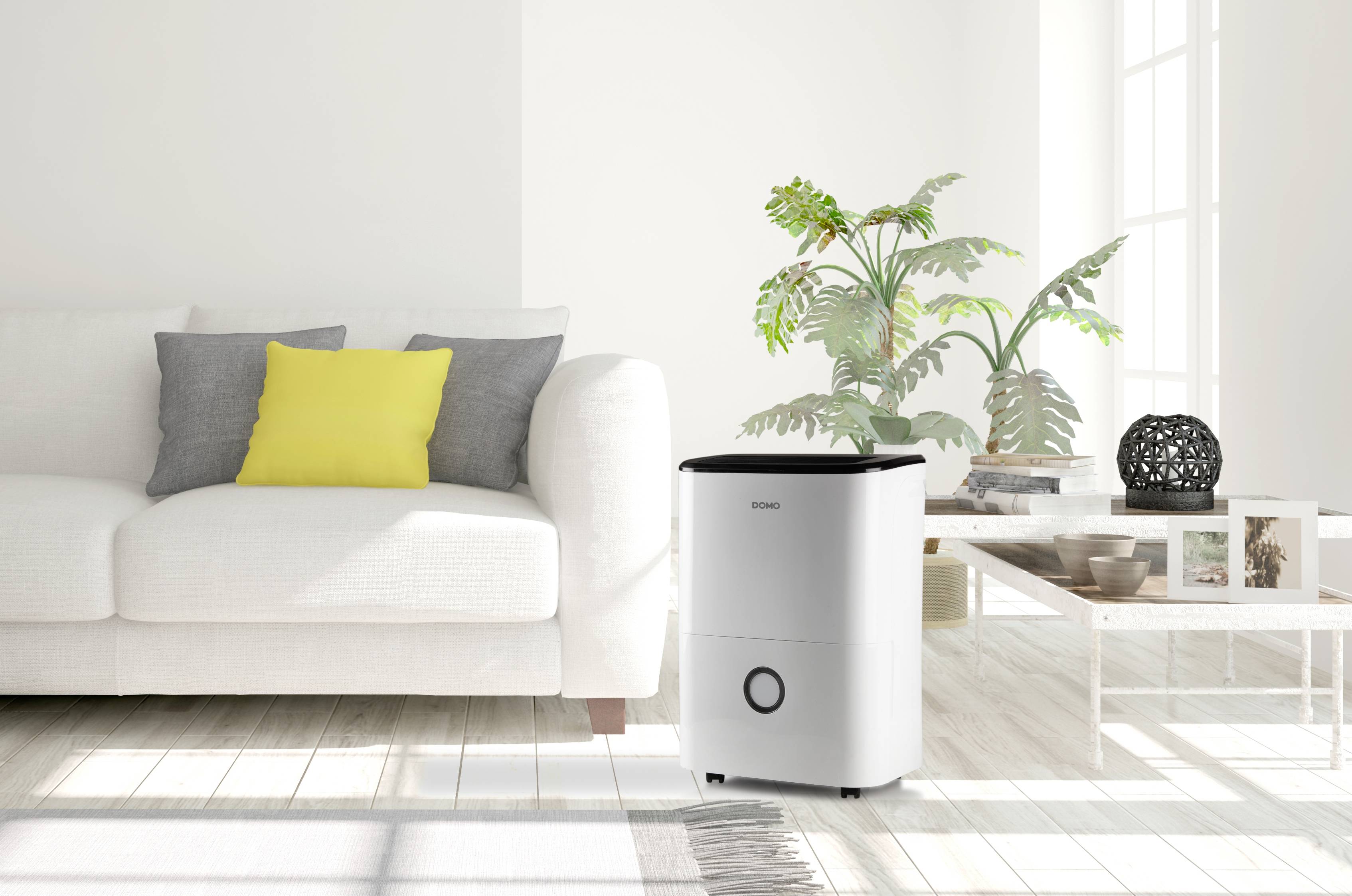 Světlý obytný prostor s bílou pohovkou, žlutým polštářem, rostlinami na stole a odvlhčovačem vzduchu na podlaze.