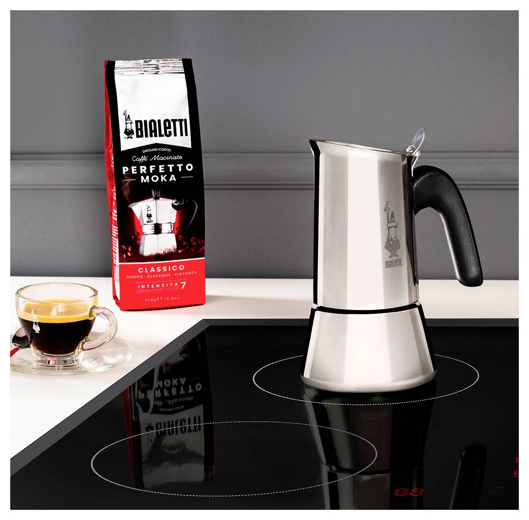 Moka konvice na indukční varné desce, vedle které stojí šálek espresa a balení s nápisem 'Bialetti Perfetto Moka'.