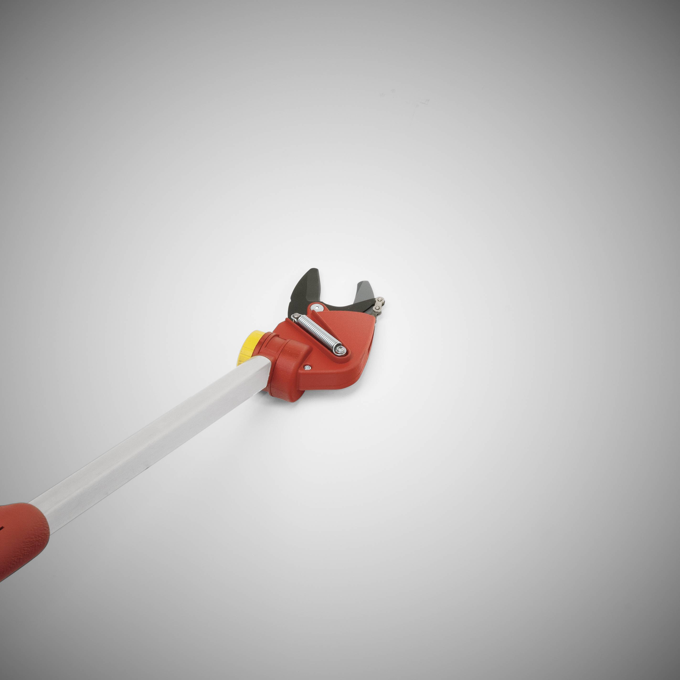 Červený a bílý teleskopický zahradnický přestřihový nástroj s ostrou čepelí na konci dlouhé rukojeti, umístěný na šedém pozadí.