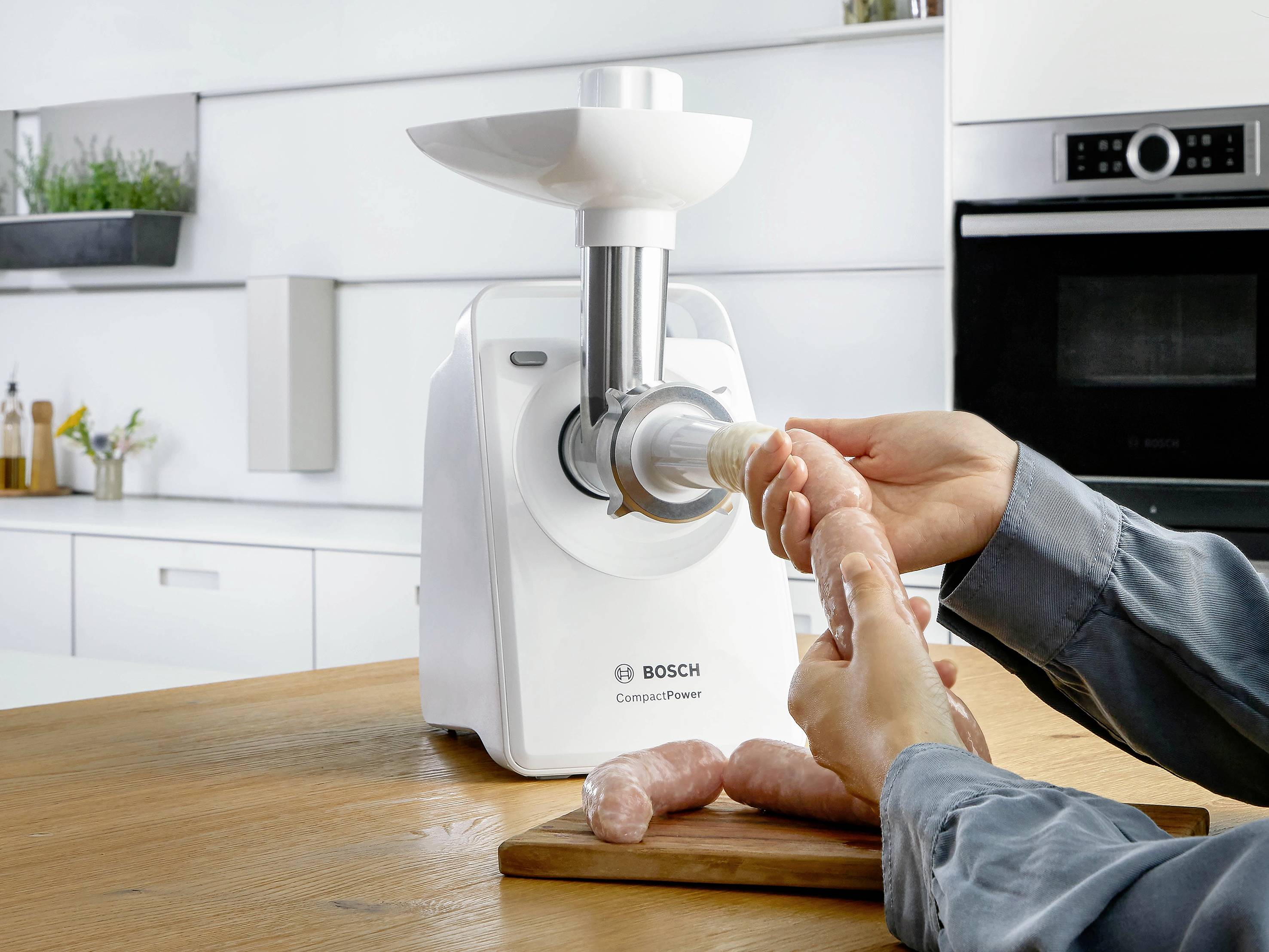 Osoba plní uzeninu na dřevěné desce pomocí Bosch mlýnku na maso v moderní kuchyni.