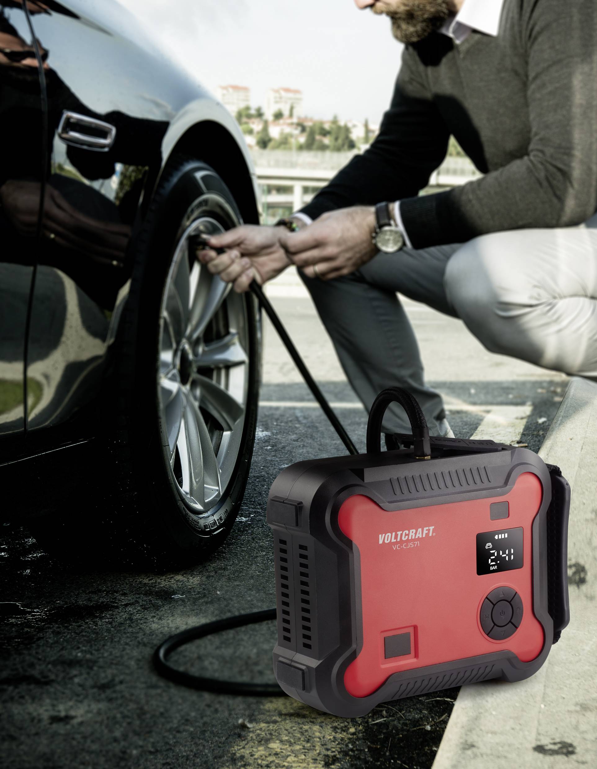 Muž doplňuje vzduch do pneumatiky automobilu přenosným červeným kompresorem na městském parkovišti.