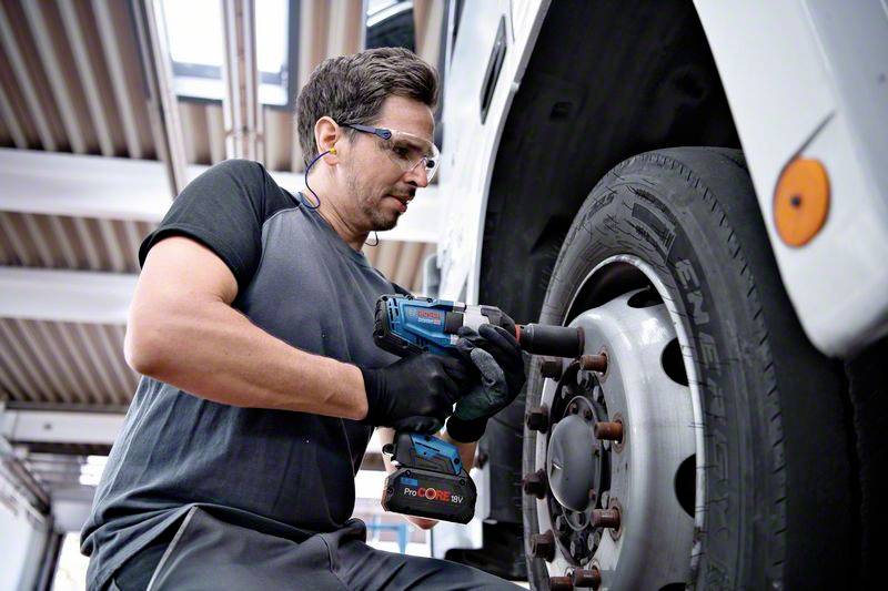 Mechanik používá elektrický rázový utahovák k utažení matic kol velkého vozidla v autoservisu.