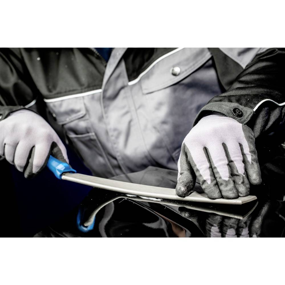 Osoba v pracovním oděvu řeže modrým nožem bílý kus materiálu na černém povrchu.