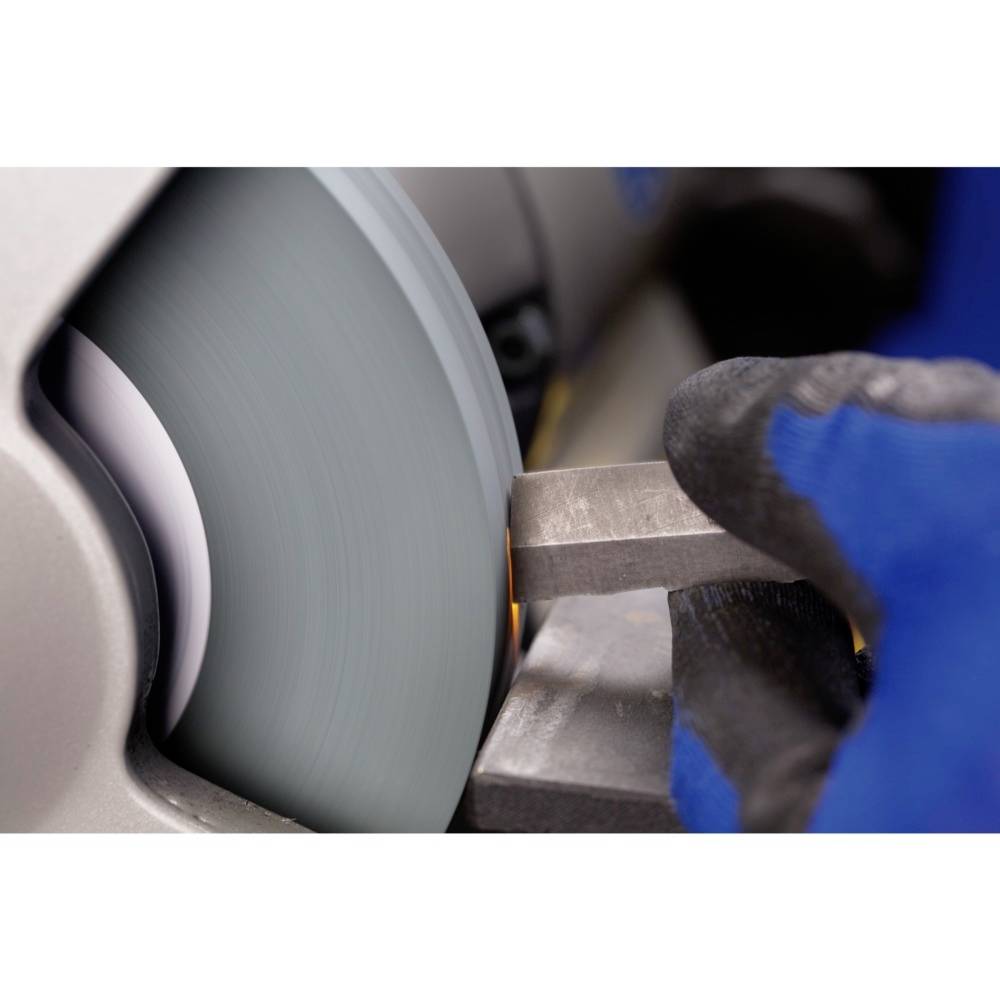 Kovová deska je opracovávána rotující brusnou kotoučí. Dělník má pro bezpečnost nasazen modrý rukavici.