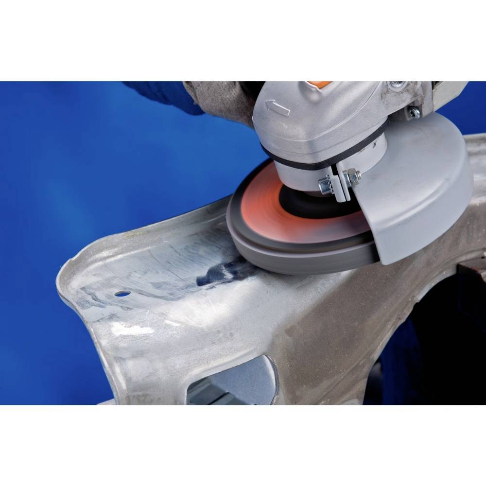 Elektrická bruska obrábí povrch kovové součástky. Pozadí je modré.