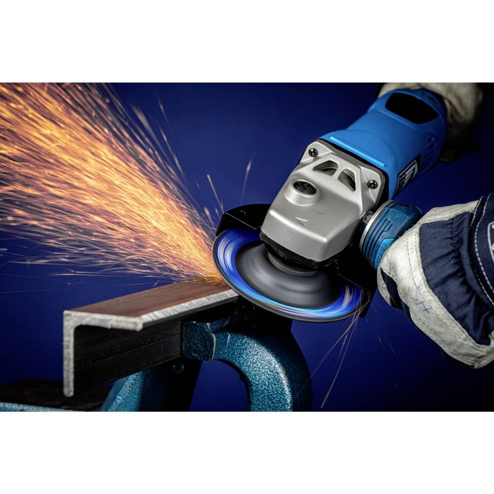 Úhlová bruska obrábí kovový díl upnutý ve svěráku, přičemž létají jiskry. Osoba má na sobě pracovní rukavice a modré oblečení.