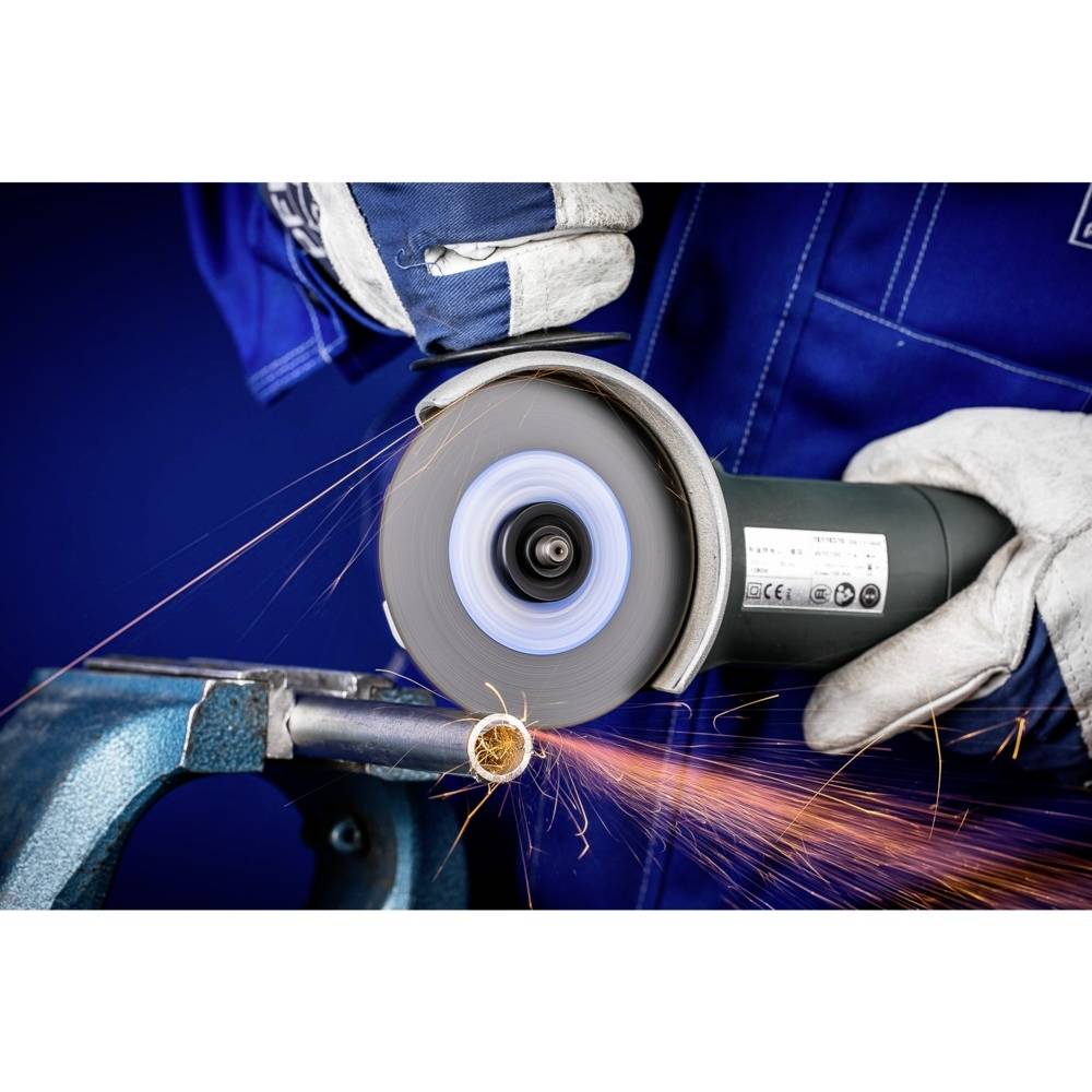 Osoba v ochranném oděvu řeže kov úhlovou bruskou. Od místa kontaktu odlétávají jiskry.