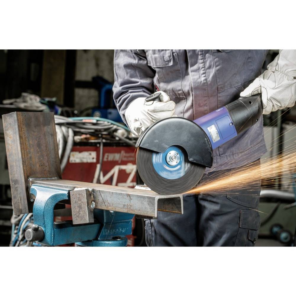 Dělník řeže kovový materiál kotoučovou pilou, přičemž létají jiskry. Je oblečen v ochranném oděvu a má rukavice v dílně.