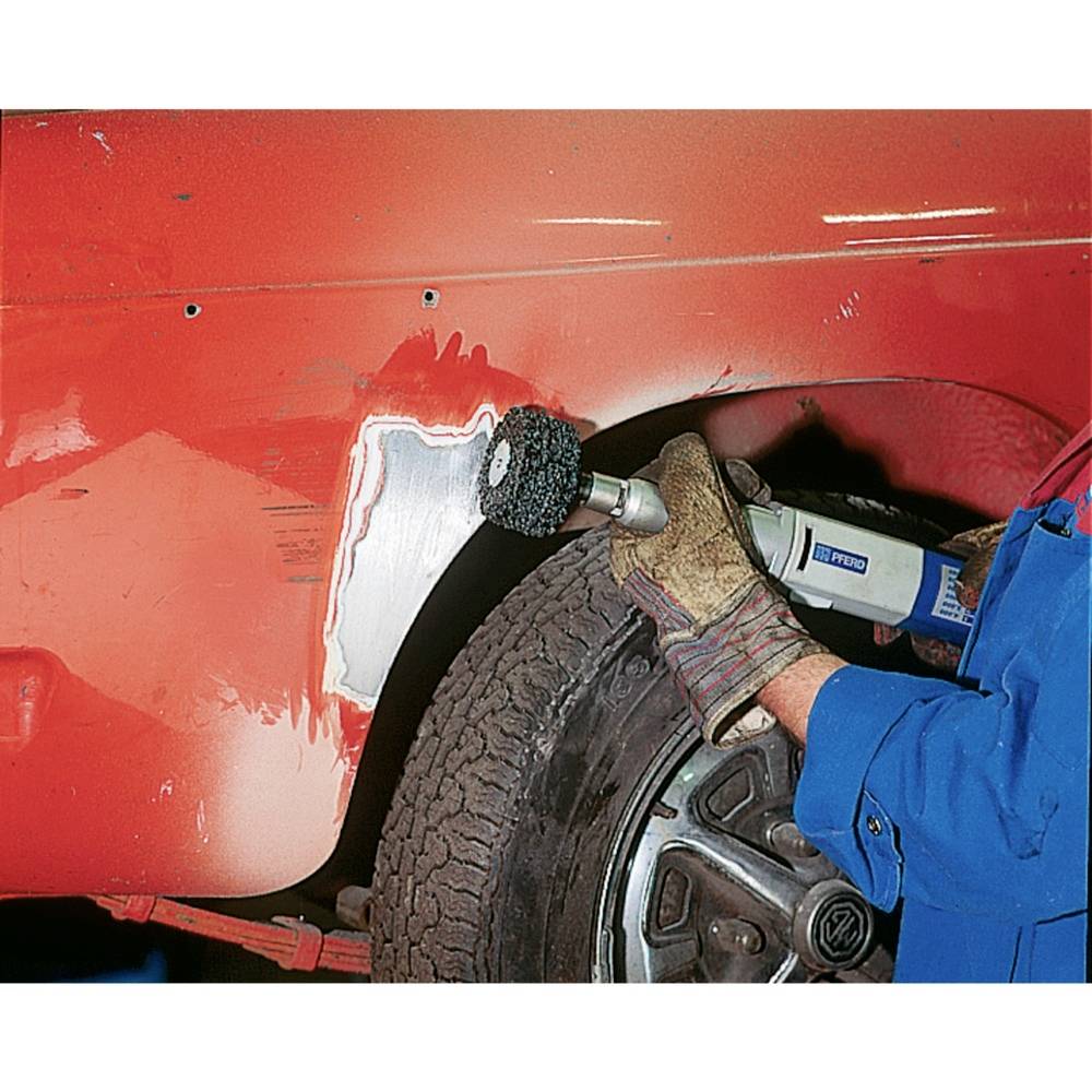 Osoba používá stroj k odstranění rzi z červené součásti automobilu. Auto je umístěno na místě s dostatečným osvětlením.