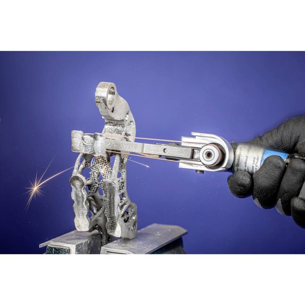 Letí jiskry, když ruka s nástrojem opracovává kovový kus. V pozadí je modrá obloha.