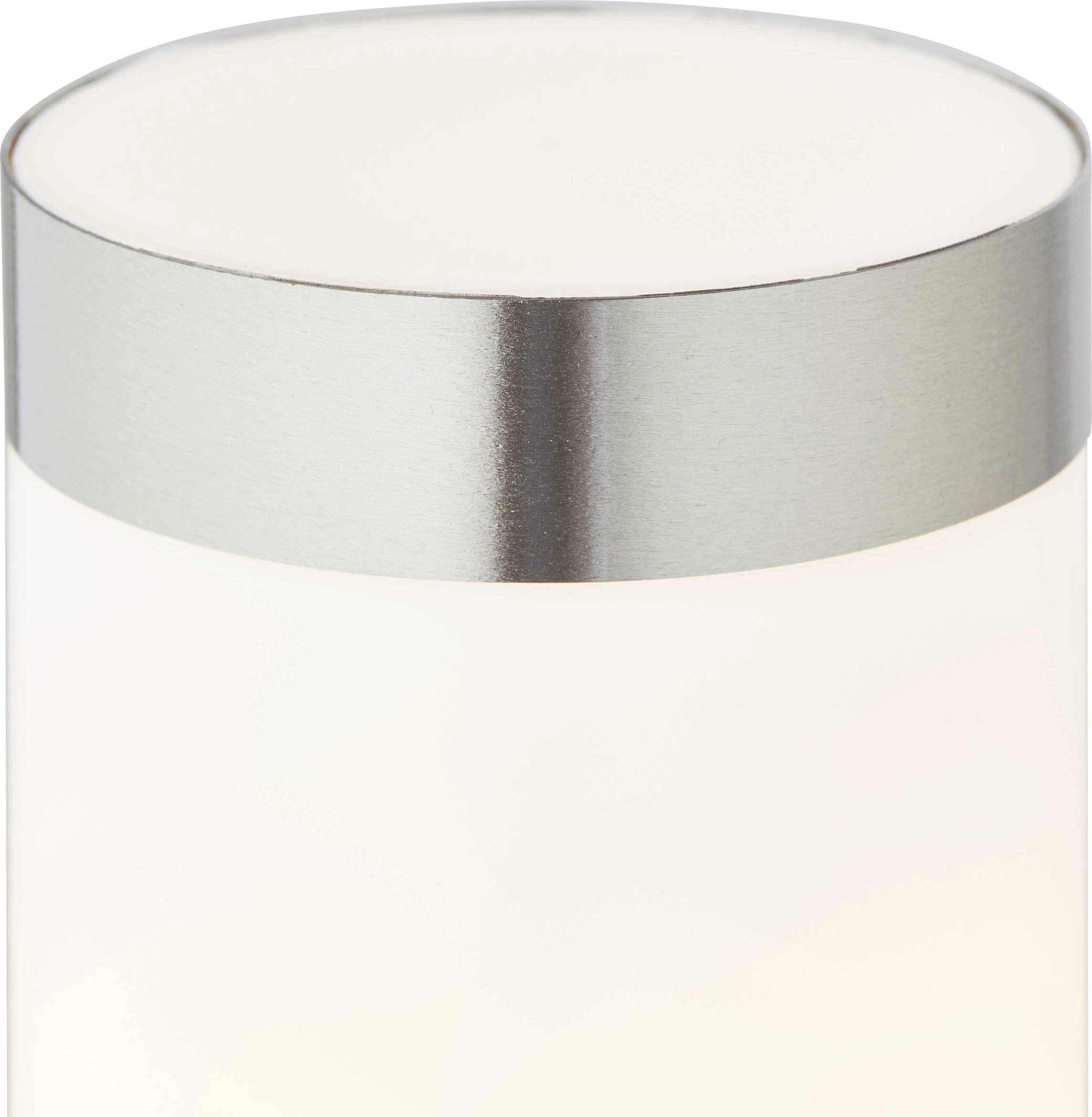 Moderní stolní lampa s válcovým bílým stínidlem a stříbrným okrajem, která vyzařuje teplé světlo.
