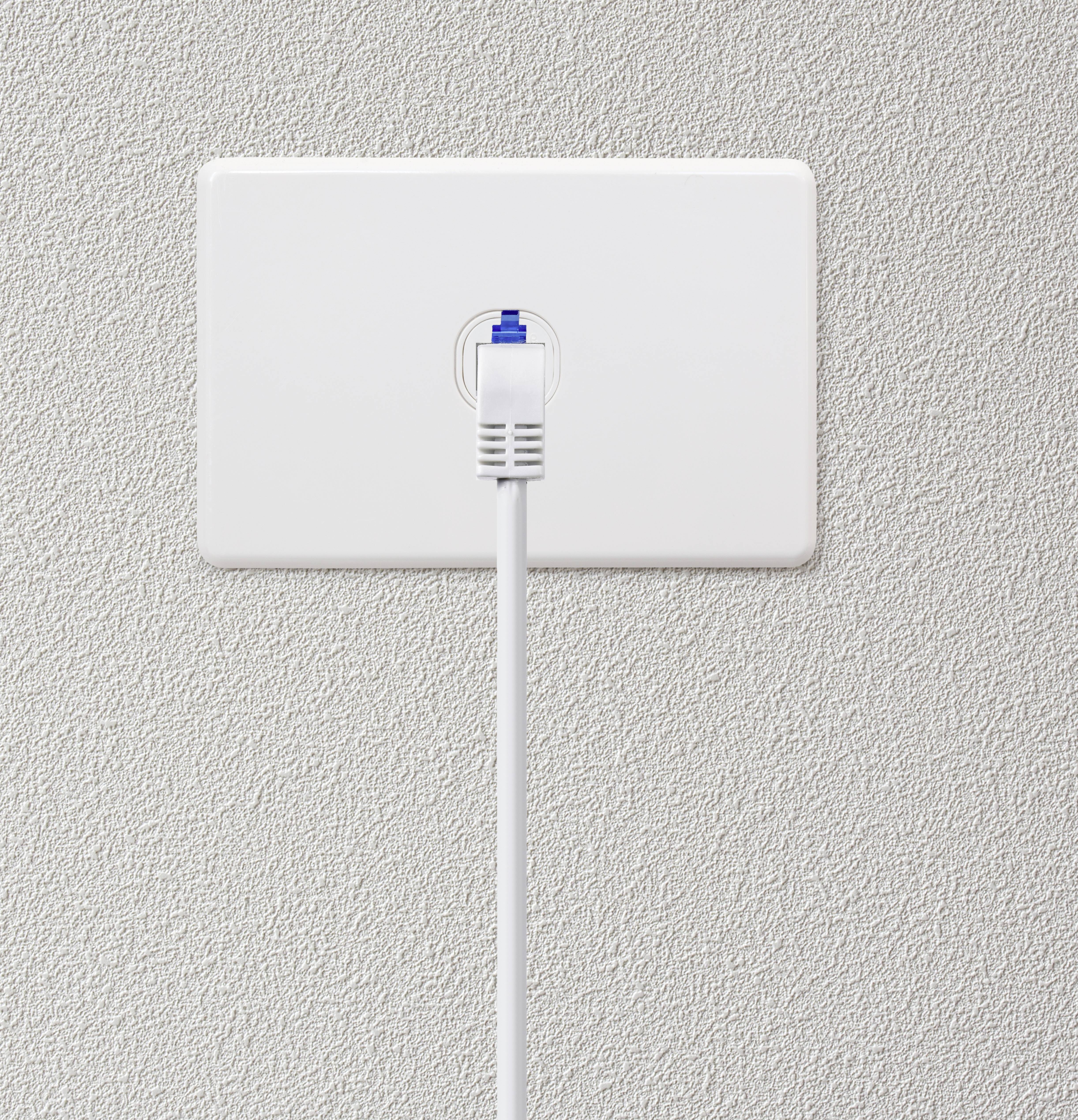 Síťový kabel je zapojen do bílé nástěnné zásuvky, kabel vede kolmo dolů.
