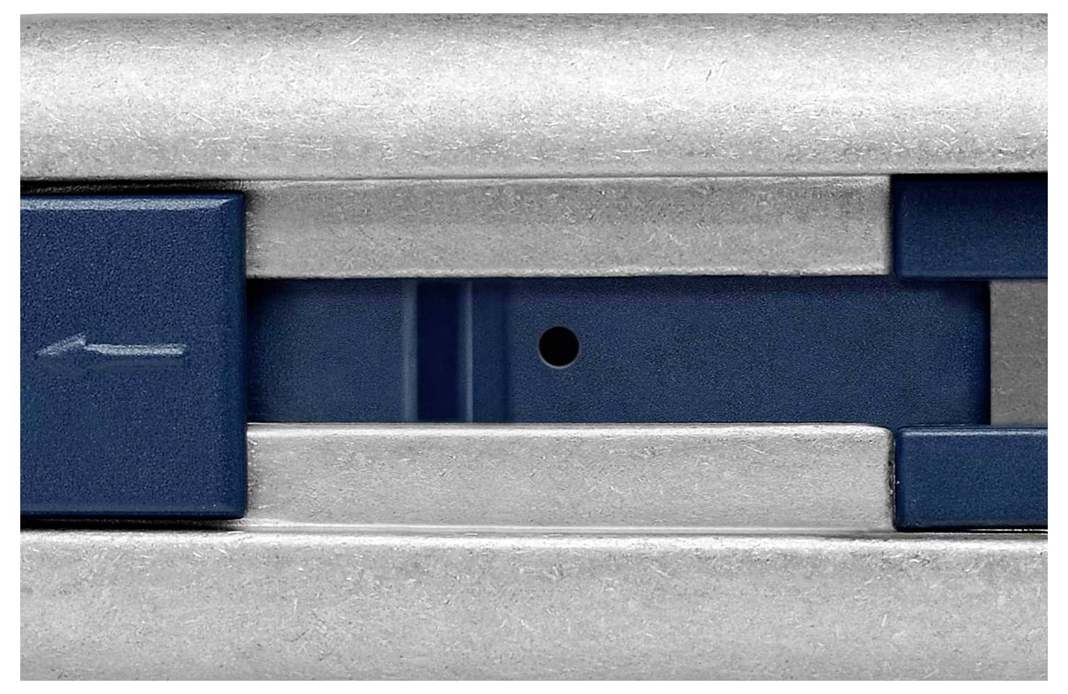 Detailní záběr kovového mechanismu s modrým posuvným ovladačem a šipkou ukazující doleva.